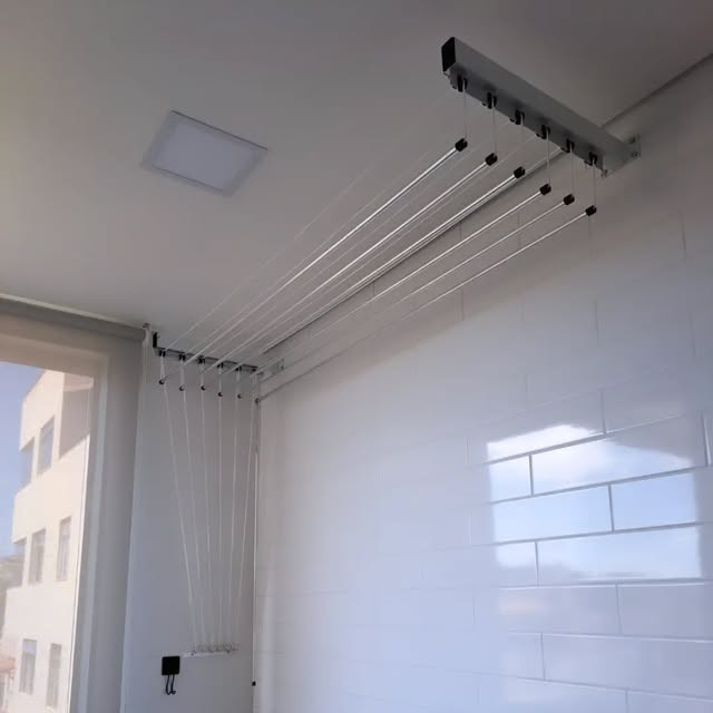 Varal de teto instalado numa área de serviço de azulejos brancos, com as cordas descendo pela parede